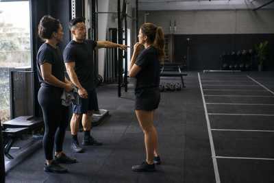 Three unbranded fitness coaches discussing an empty marked training lane after a group class