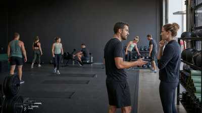 Gym coach and operations manager discussing a group class while members reset equipment in an unbranded functional training gym