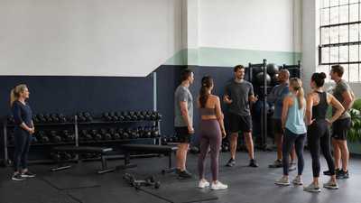 A new coach welcoming group fitness members while a site manager observes in an unbranded functional training studio